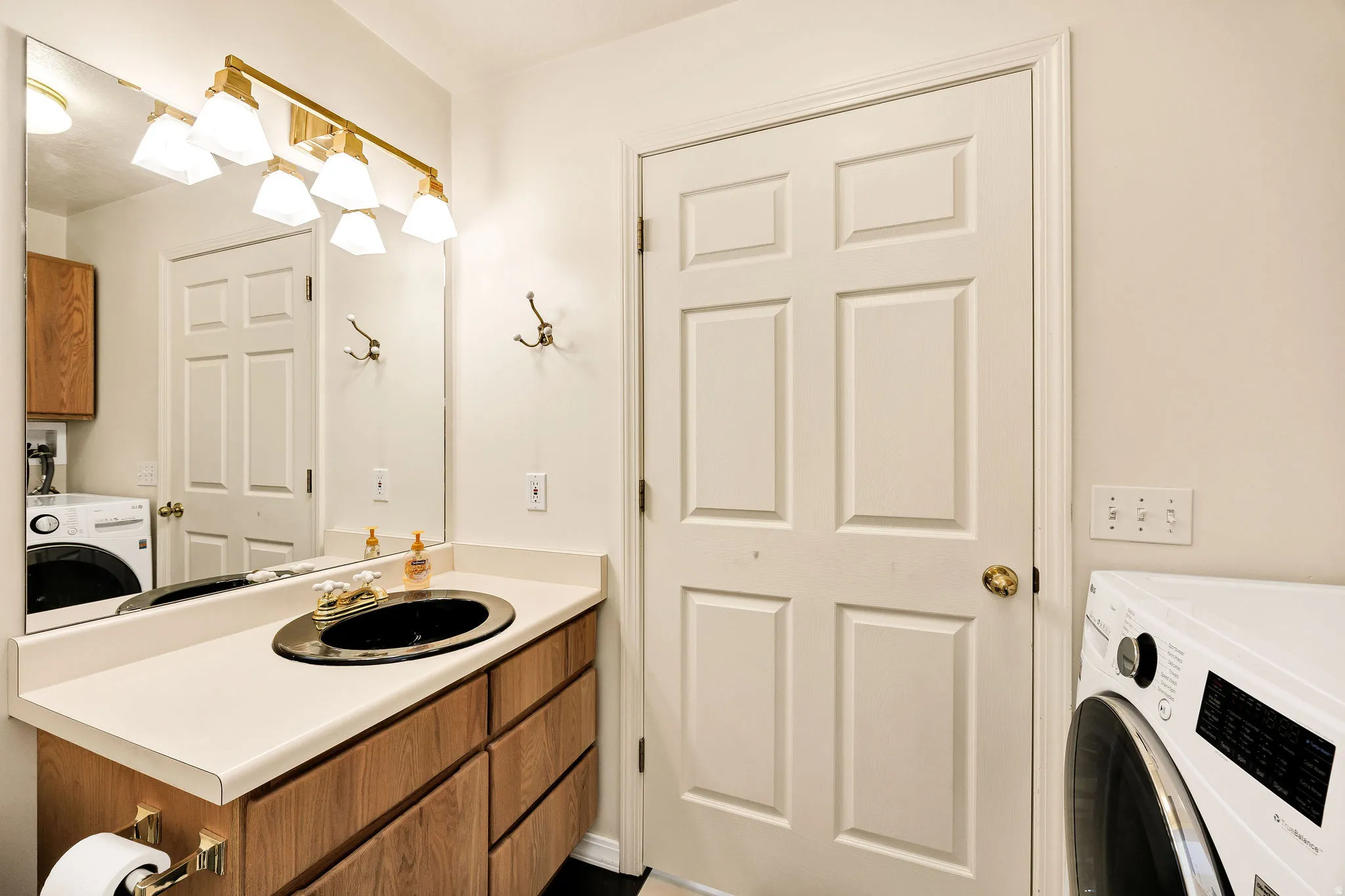 Vanity with a black oval sink, brass-finish faucet, and coordinating lighting fixture