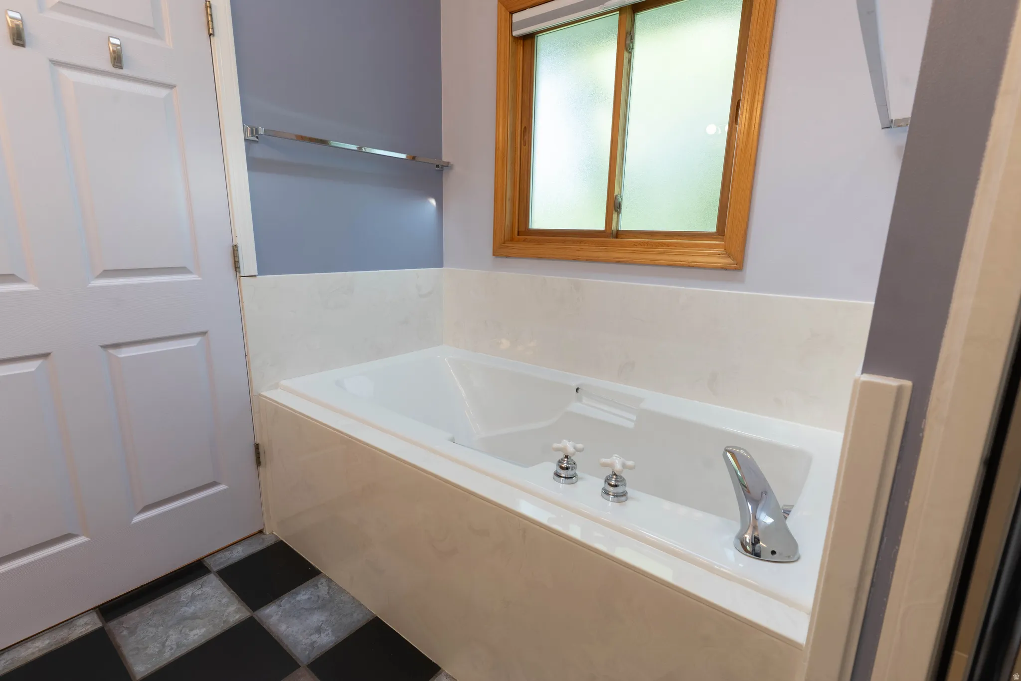 Built-in bathtub with polished chrome fixtures, wood-framed window, and checkerboard floor tiles