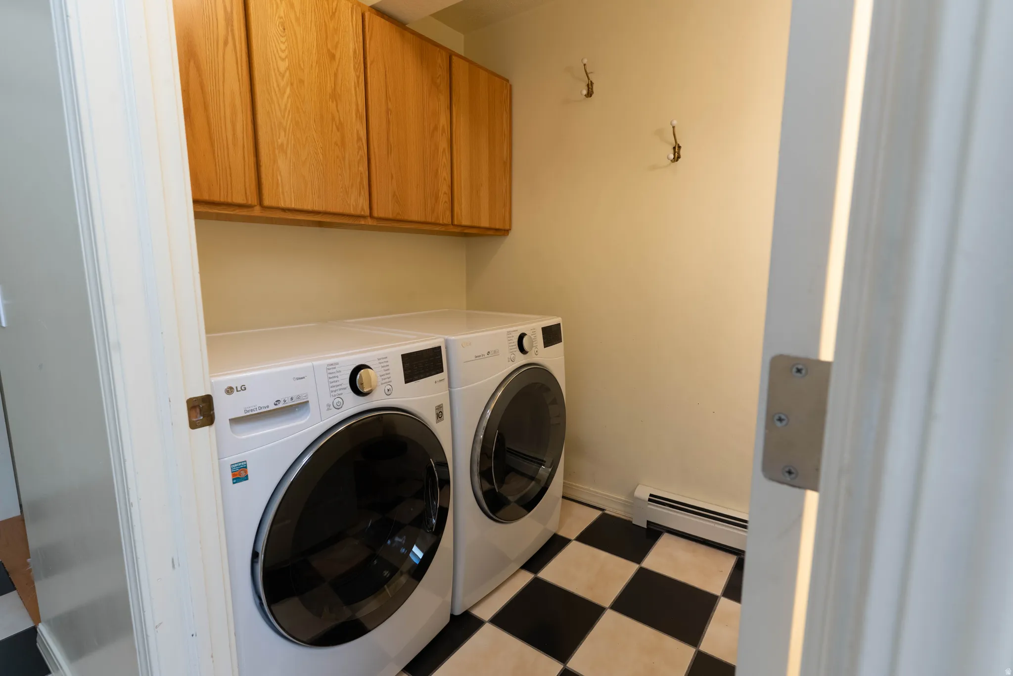 Utility area featuring checkerboard flooring, upper cabinetry, and a baseboard heater