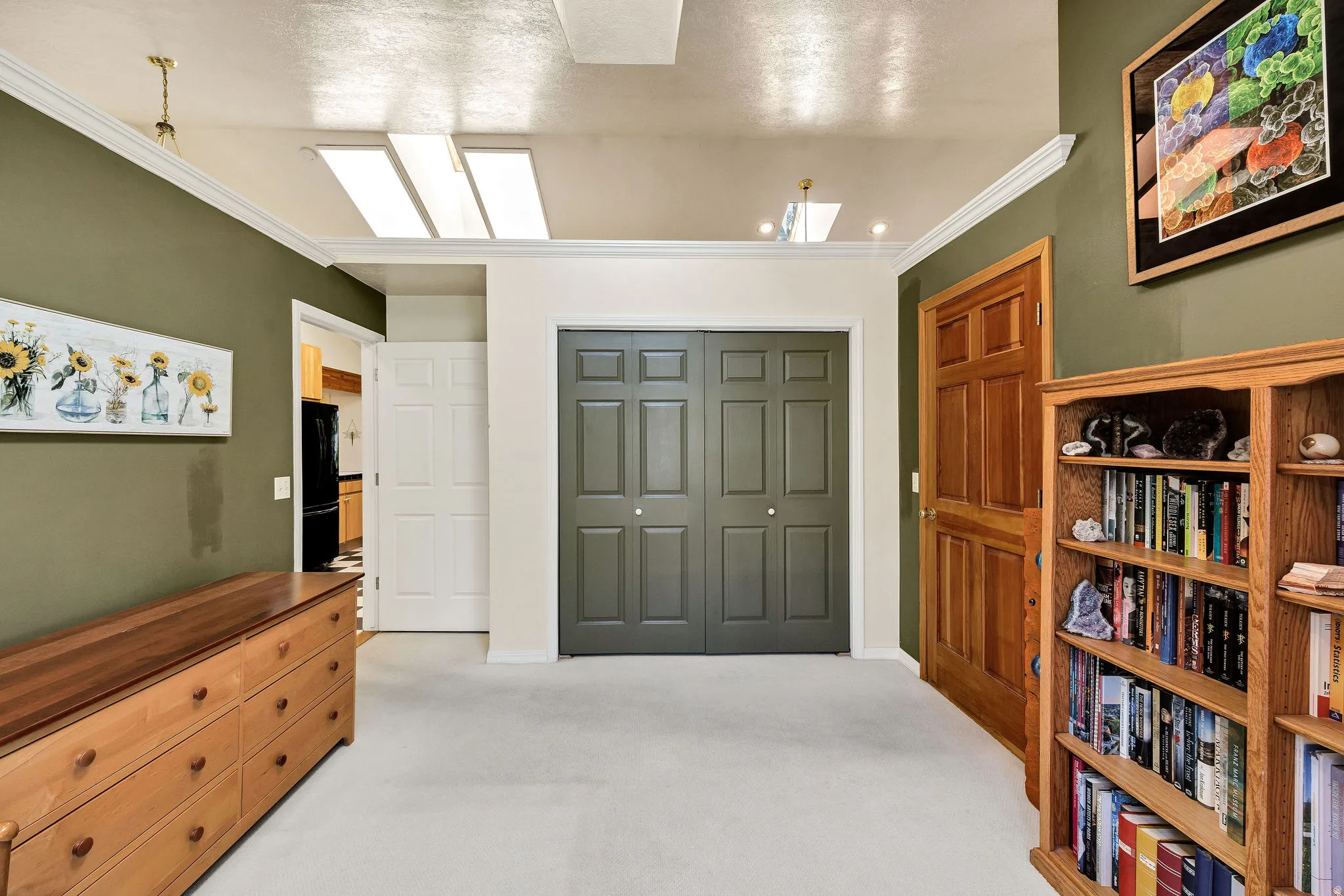 Recessed lighting with multiple skylights, carpet flooring, a natural wood paneled door, and a two-panel bifold closet door