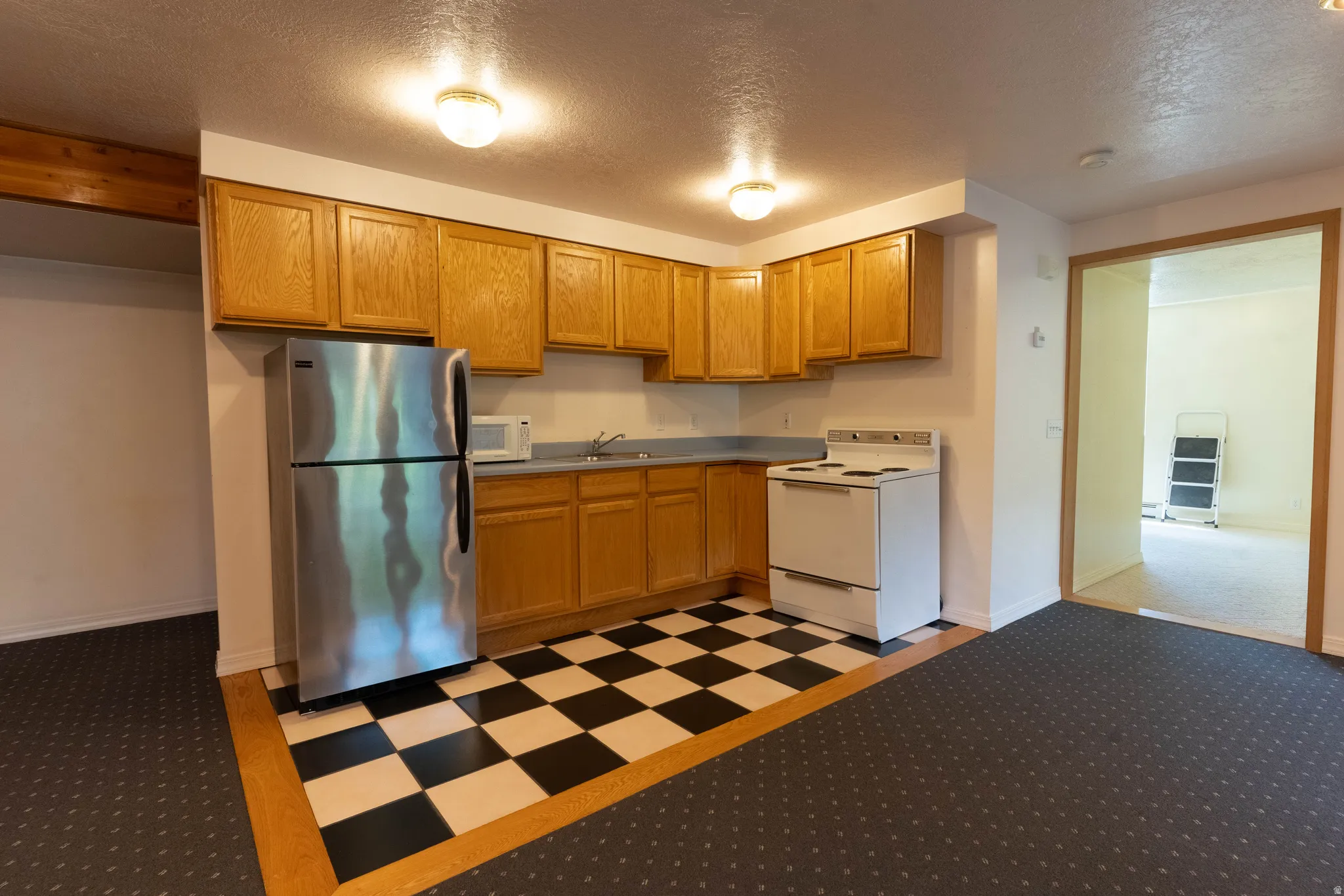 Kitchenette with wood-finish cabinetry, stainless steel refrigerator, white electric range, and checkerboard floor tiles