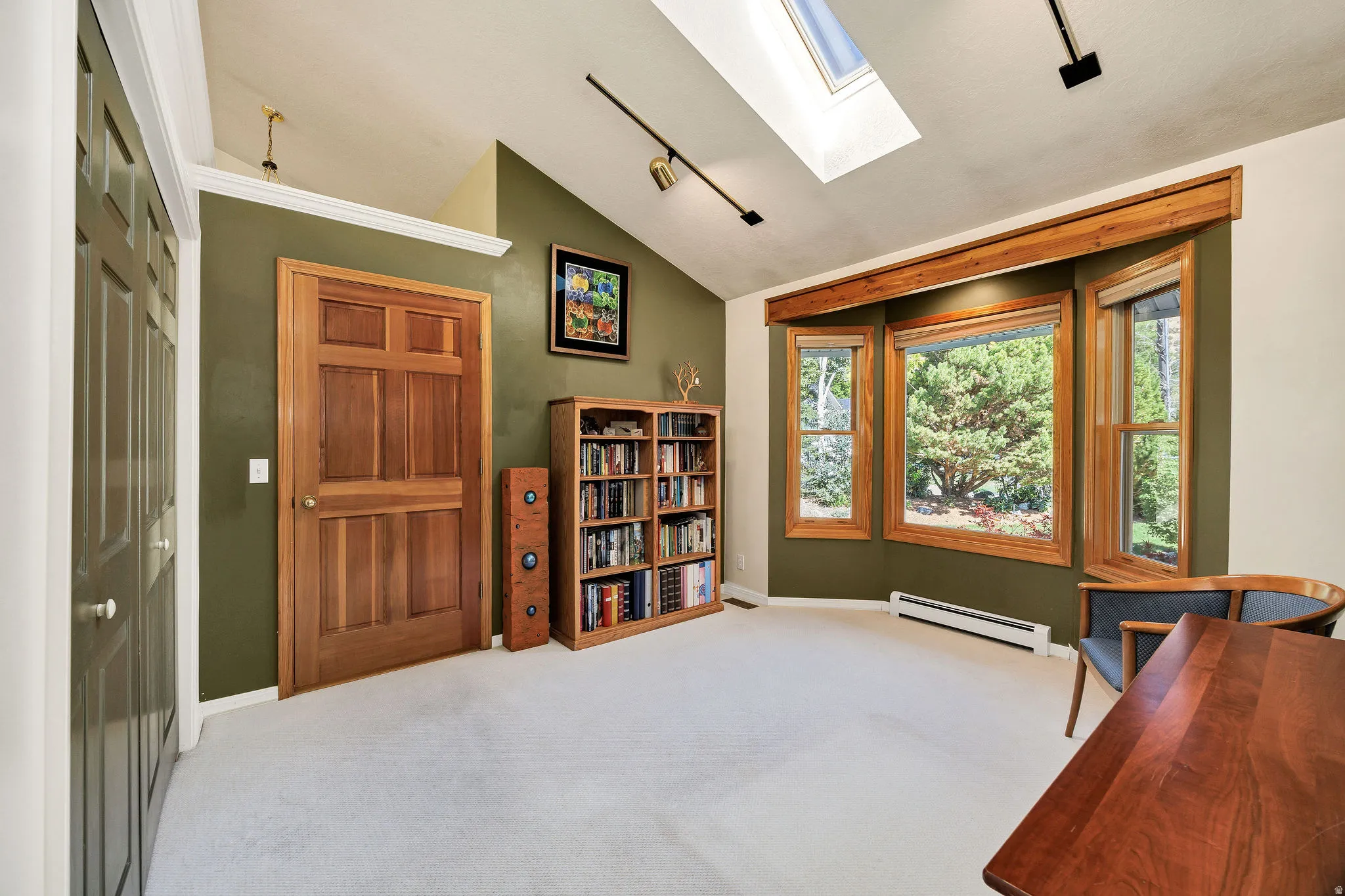 Vaulted ceiling with skylight, wood-frame bay windows, built-in shelving, natural wood doors, and track lighting