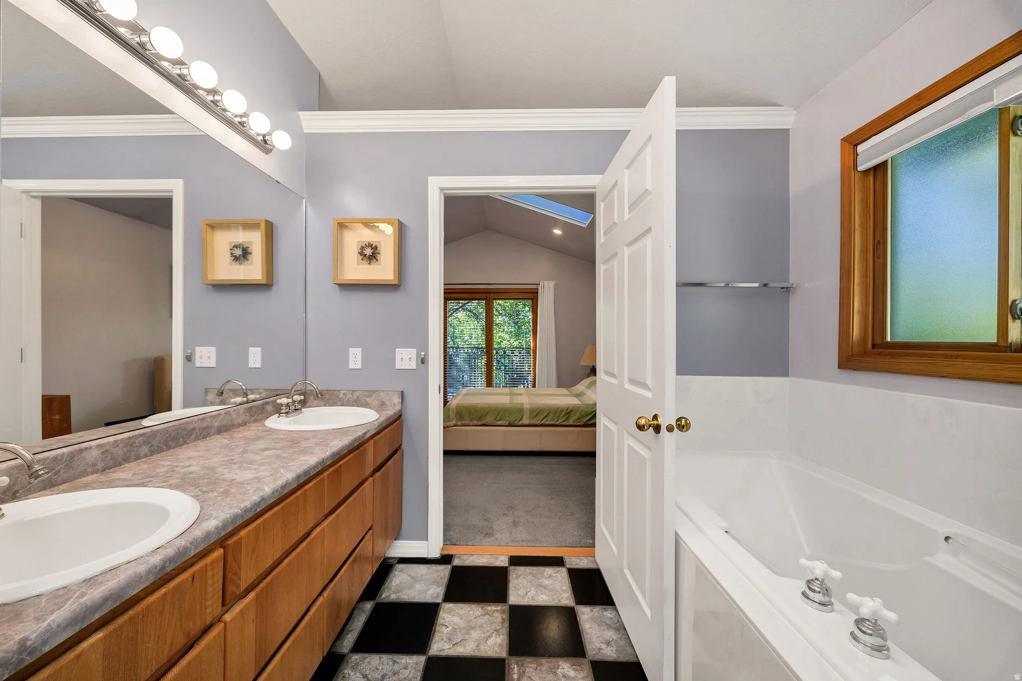 Dual vanity with undermount sinks, wood-finish cabinetry, vanity mirror with overhead lighting, and a built-in bathtub with chrome fixtures