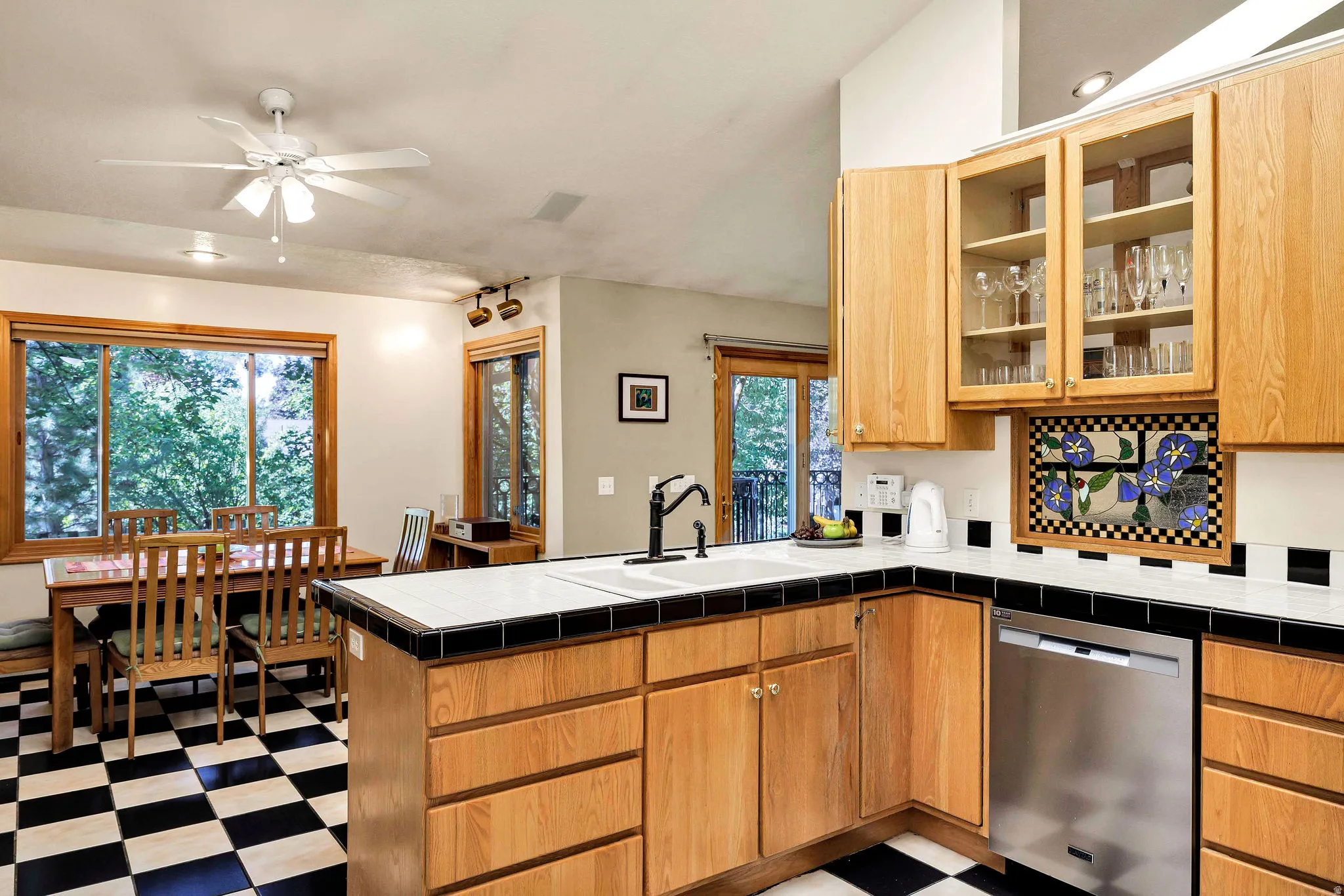 Kitchen with wood-finish cabinetry, tile countertops, stainless steel dishwasher, and checkered floor