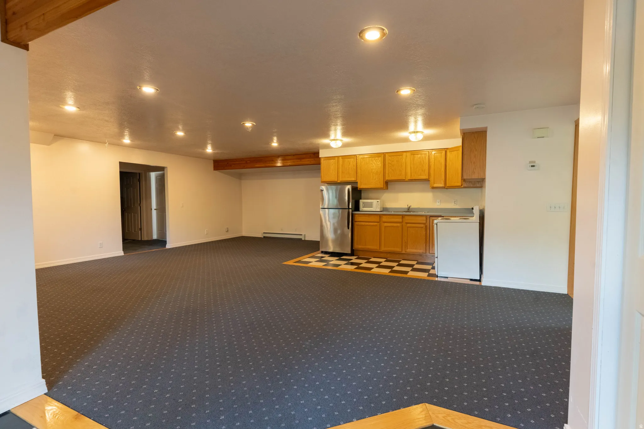 Expansive room featuring recessed lighting, a built-in kitchenette with wood cabinetry, checkered flooring, and carpet