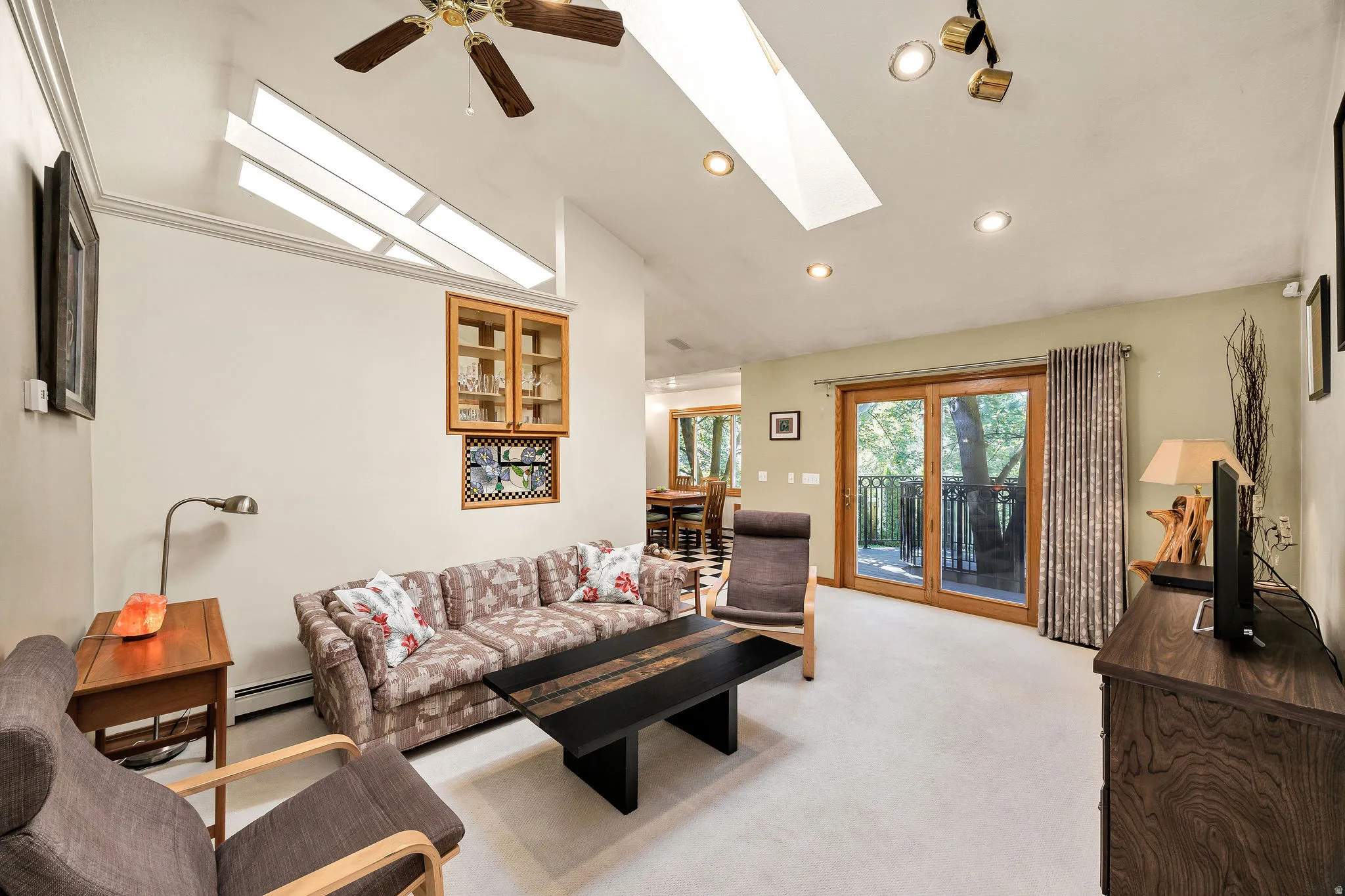 Vaulted ceiling with skylights, recessed lighting, wood-finish ceiling fan, built-in cabinetry, and sliding glass door with balcony access