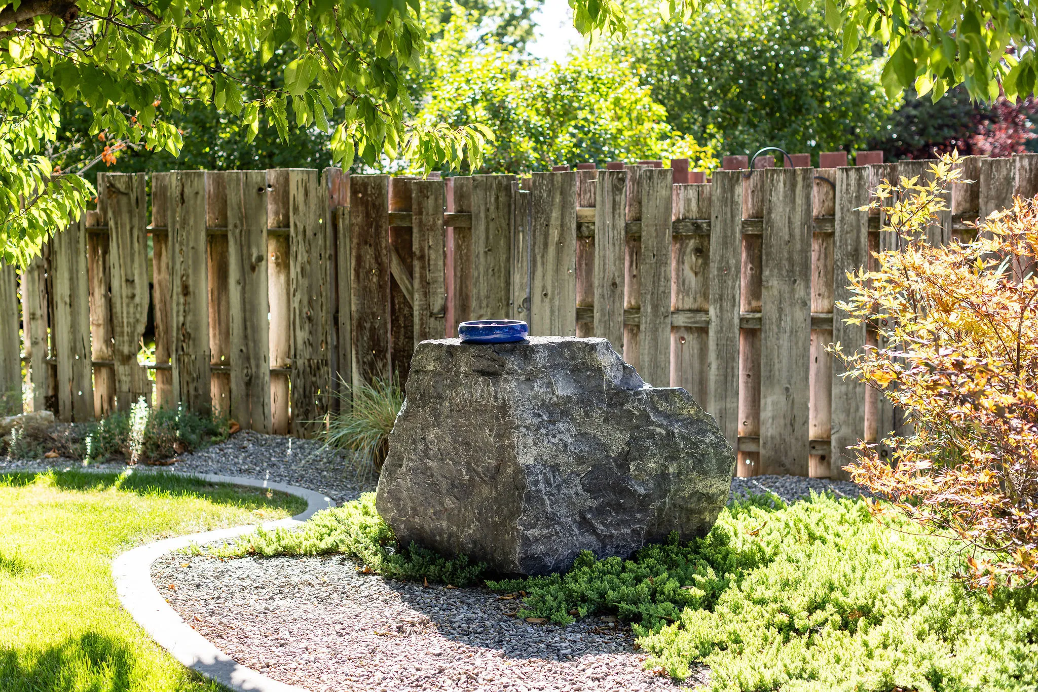 Landscaped garden area featuring a natural stone boulder, gravel ground cover, and a decorative wooden fence