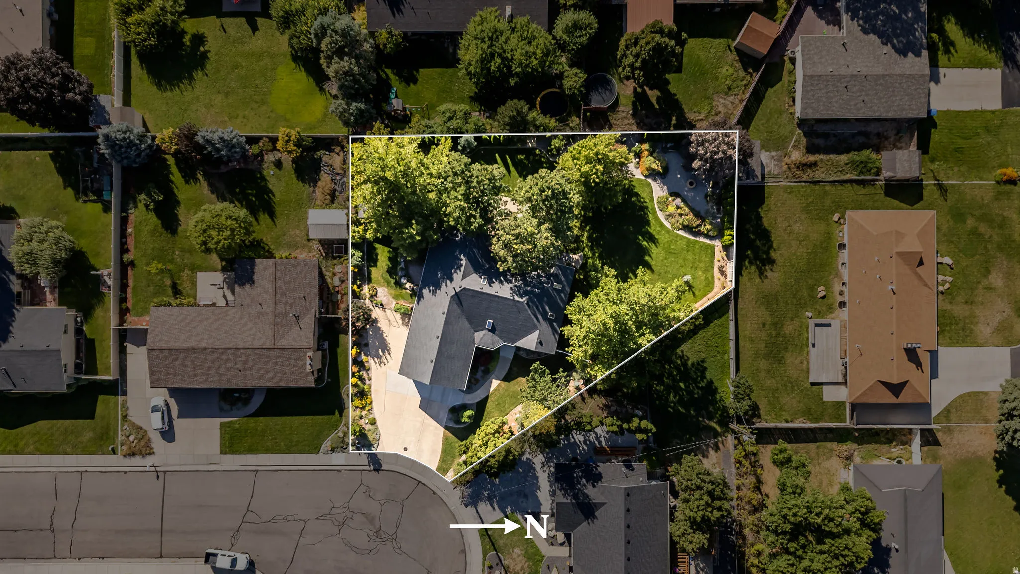 Asphalt shingle roof, curved driveway, mature trees, expansive green lawn, and clearly defined property boundaries