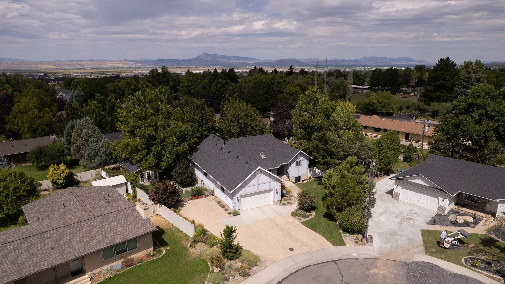 Aerial perspective highlighting a residential property with a dark shingle roof and an attached garage