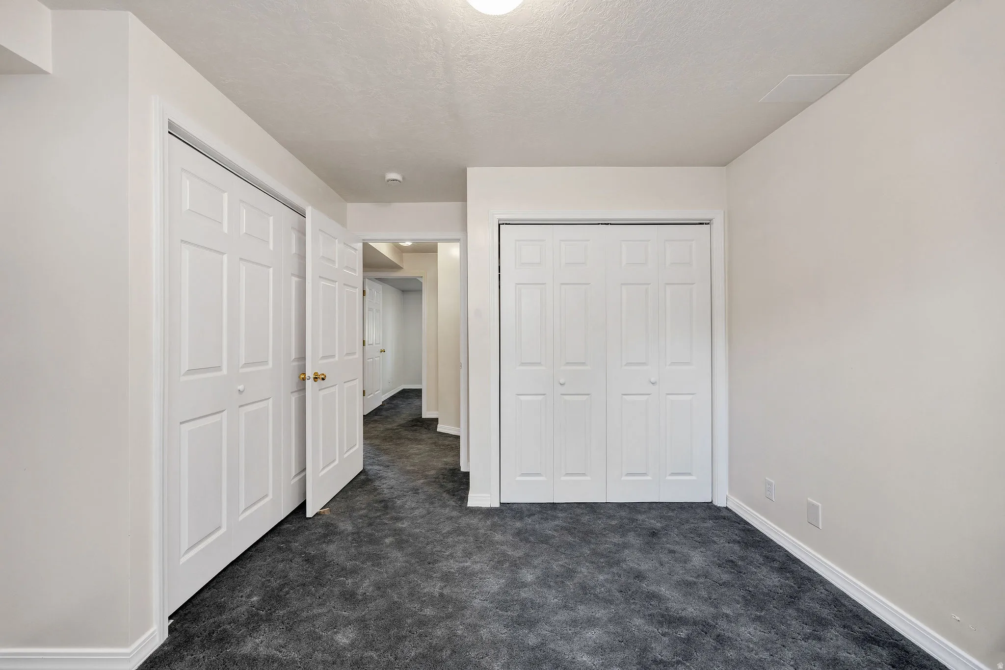 Neutral wall paint and ceiling, dark textured carpeting, white baseboards, and two sets of white bi-fold doors