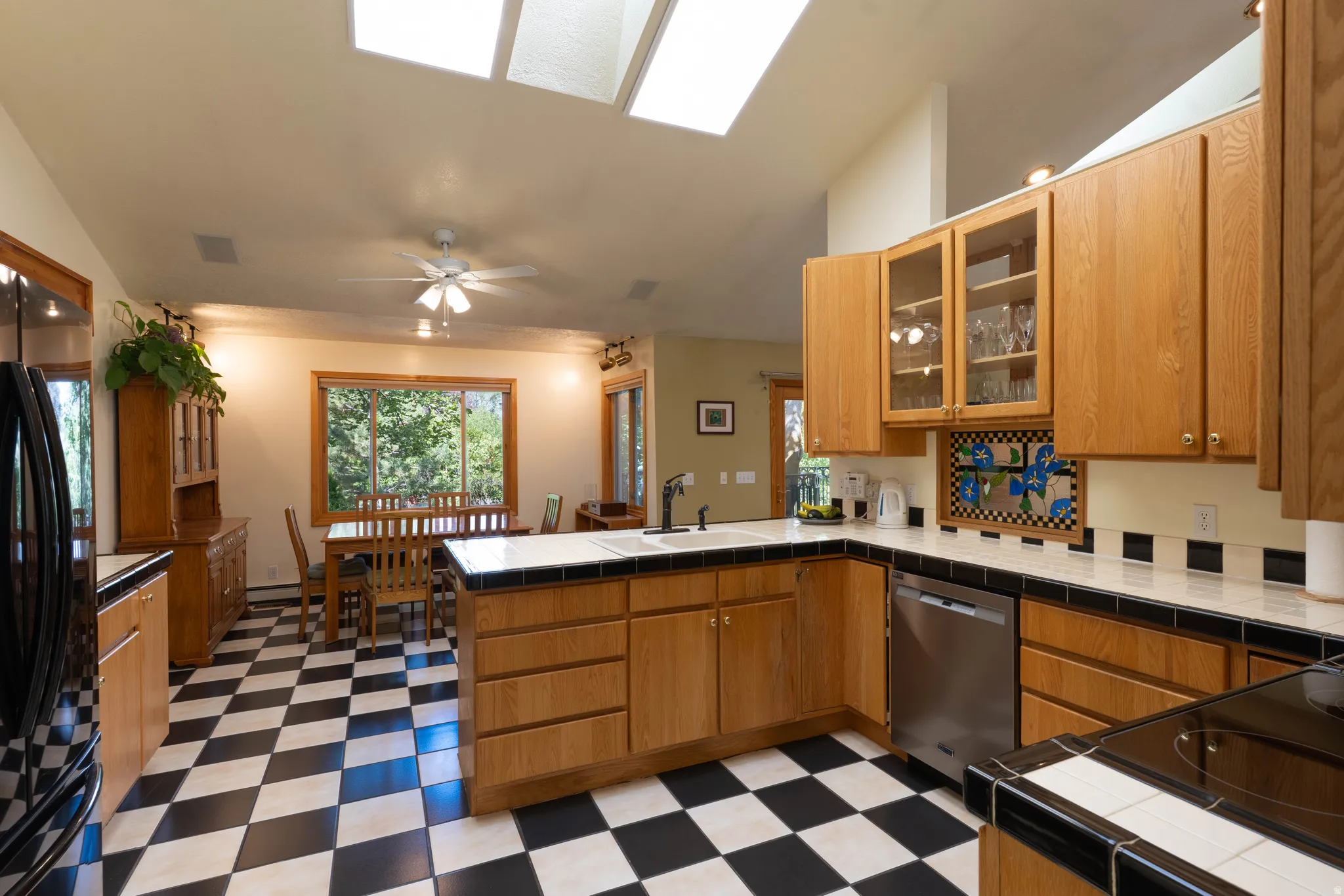 Kitchen featuring skylights, wood-finish cabinetry, black and white checkerboard flooring, a built-in dishwasher, and a dining area with a large window