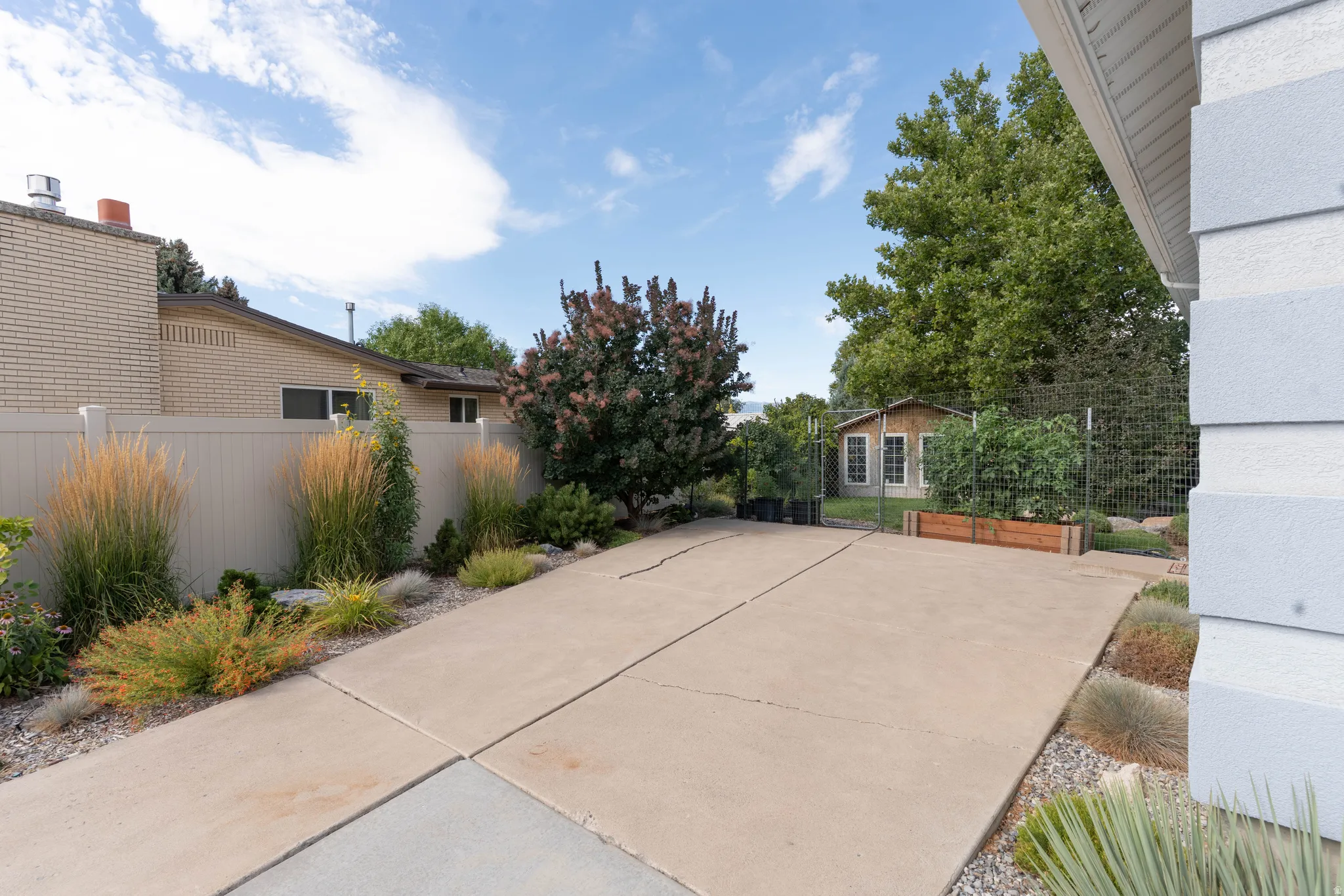 Paved concrete surface with surrounding landscaping, a raised garden bed, and an outbuilding