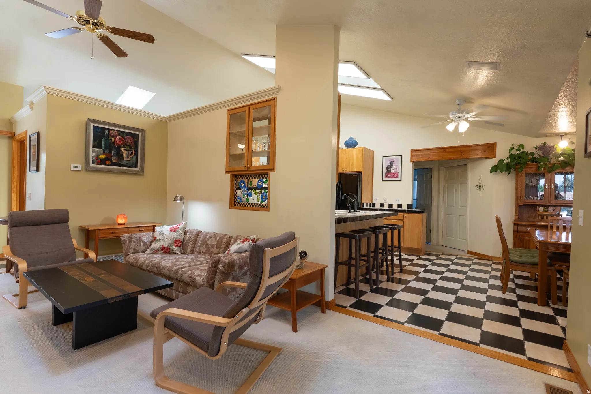 Vaulted ceilings with skylights, ceiling fans, built-in cabinetry, breakfast bar with seating, and checkered flooring