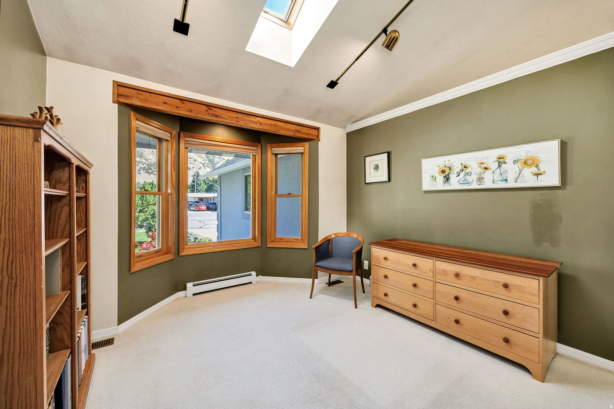 Skylight with track lighting, bay window with wood trim, built-in shelving, crown molding, and carpeted flooring
