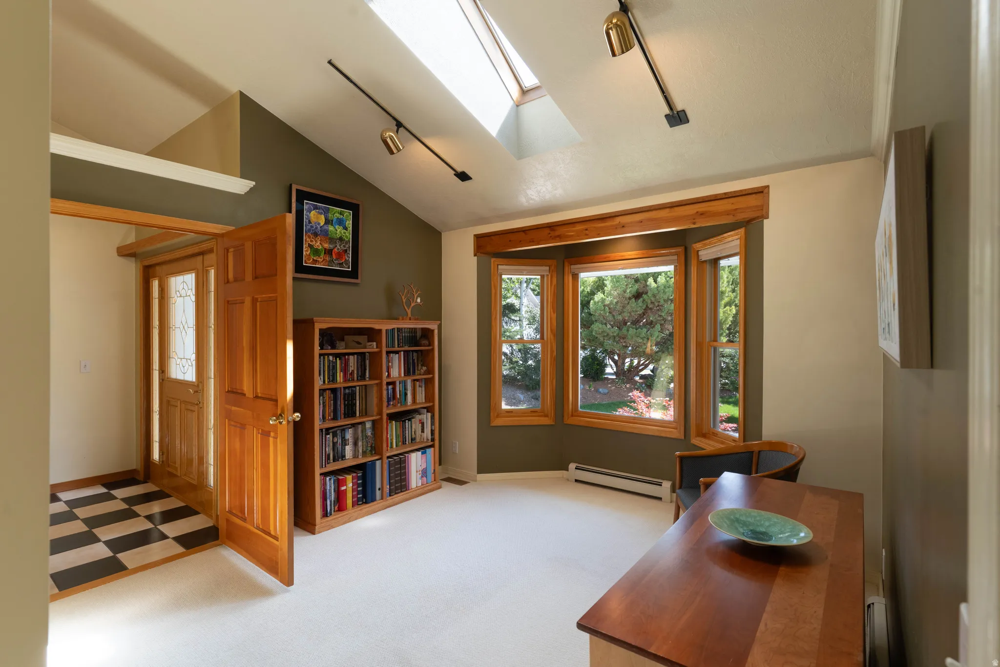 Vaulted ceilings with skylights, track lighting, wood-finish entry door with patterned glass, checkerboard tile flooring, and a bay window