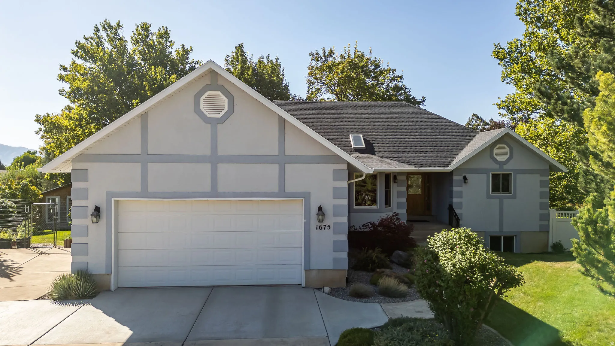 Light-toned stucco exterior with contrasting trim, gable roofline, attached two-car garage, and established landscaping