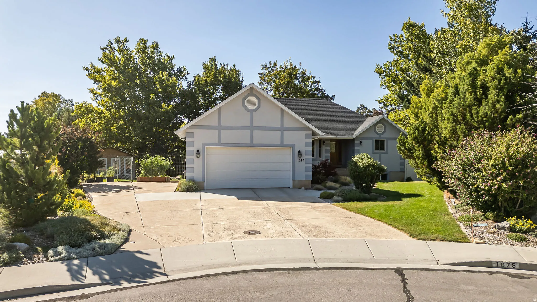 Pitched roof residence with an attached two-car garage, concrete driveway, and established landscaping