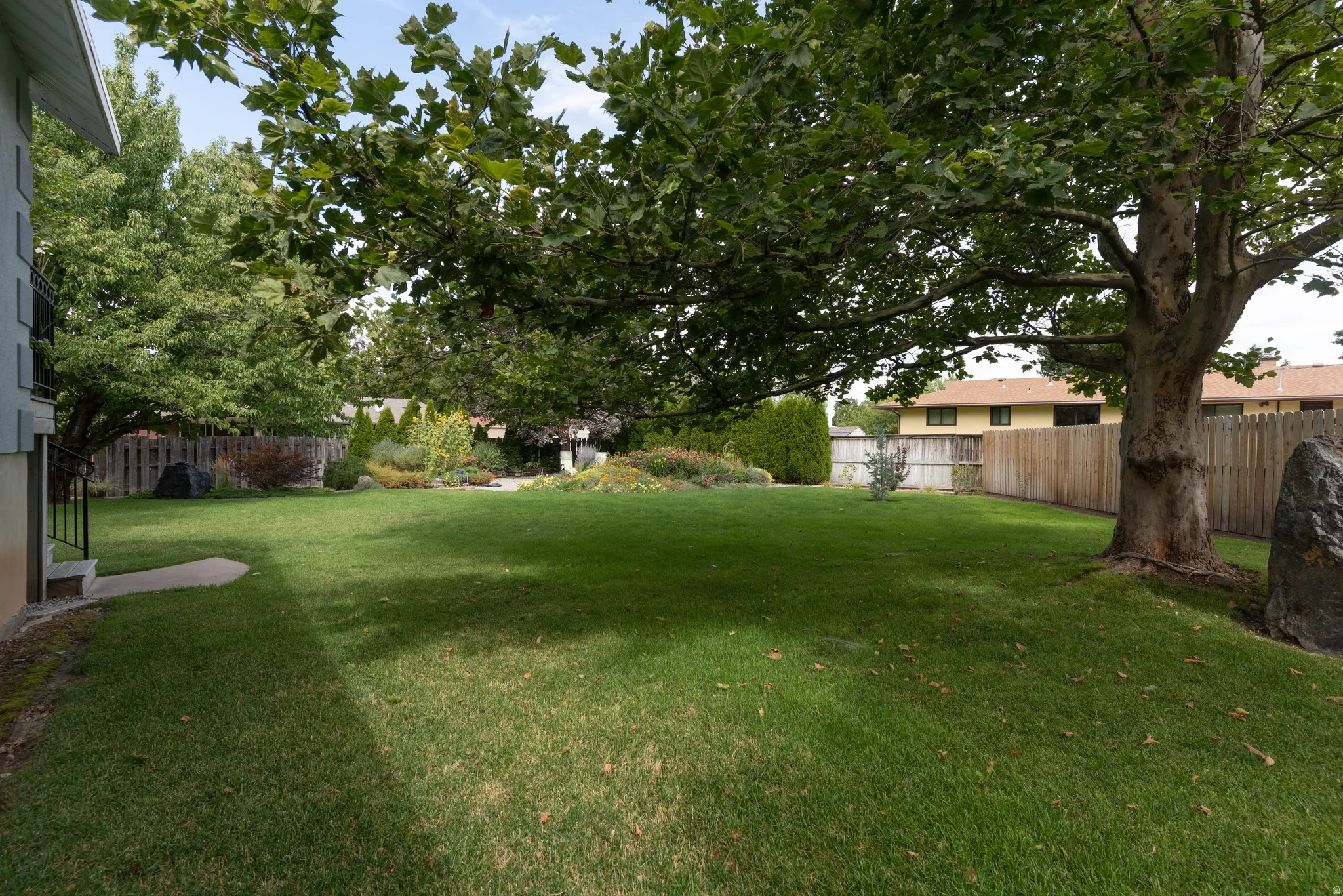 Expansive backyard featuring a manicured lawn, mature trees, and a wooden privacy fence