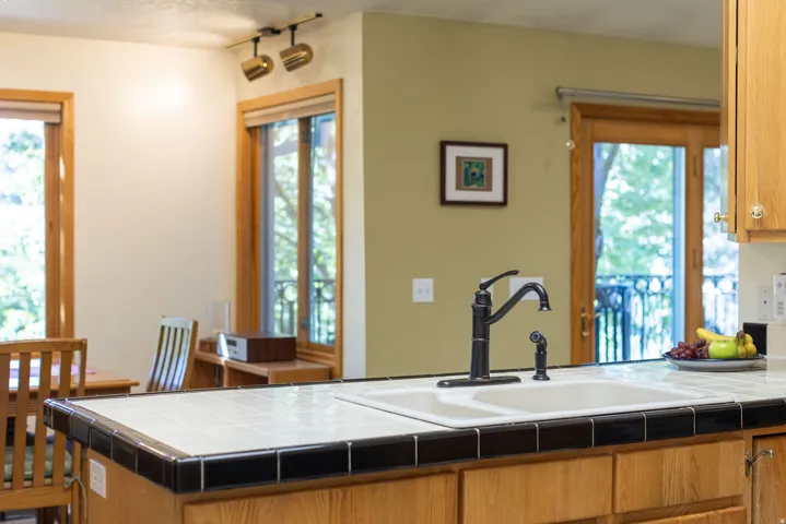 Ceramic tile countertop with black trim, stainless steel double basin sink, and oil-rubbed bronze faucet