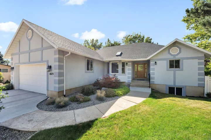 Exterior featuring a two-car garage, mature landscaping, a concrete walkway, and a wood-finish front door