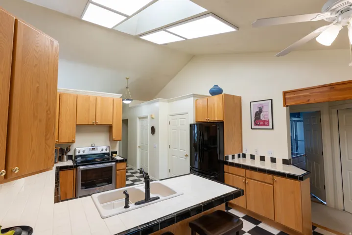 Vaulted ceiling with skylights, wood-finish cabinetry, tile countertops, black and white checkered flooring, and a ceiling fan
