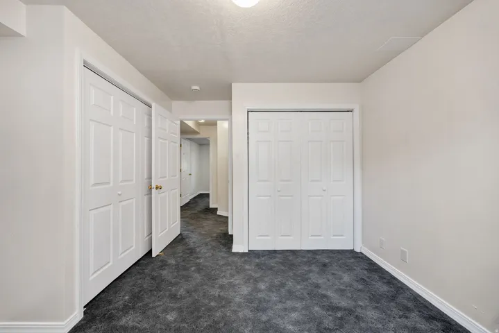 Neutral wall paint and ceiling, dark textured carpeting, white baseboards, and two sets of white bi-fold doors