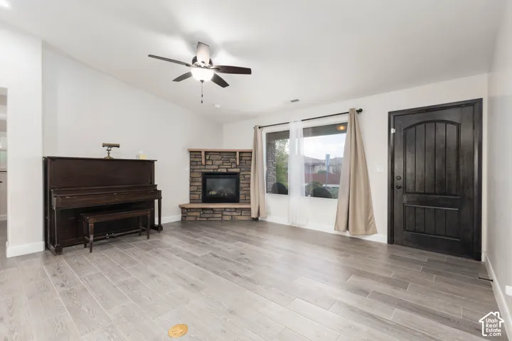 Vaulted ceilings, a stone-clad fireplace, wood-finish flooring, and a ceiling fan