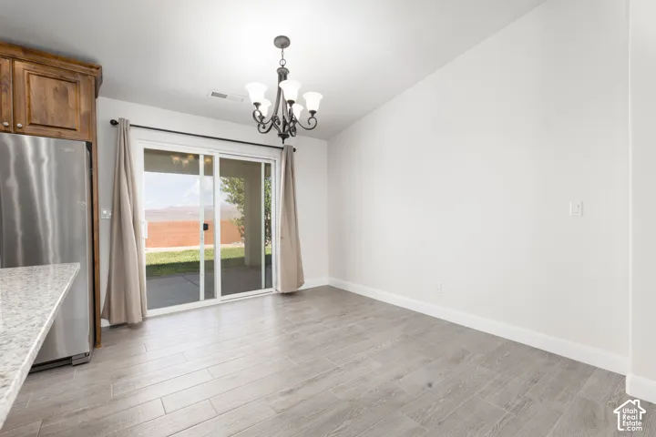 Wood-finish flooring, sliding glass door, overhead chandelier, light-toned walls, and a granite-style countertop