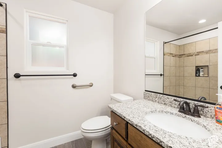 Bathroom featuring a granite-finish vanity, dark wood-finish cabinetry, a framed mirror, and a tiled shower with an integrated niche