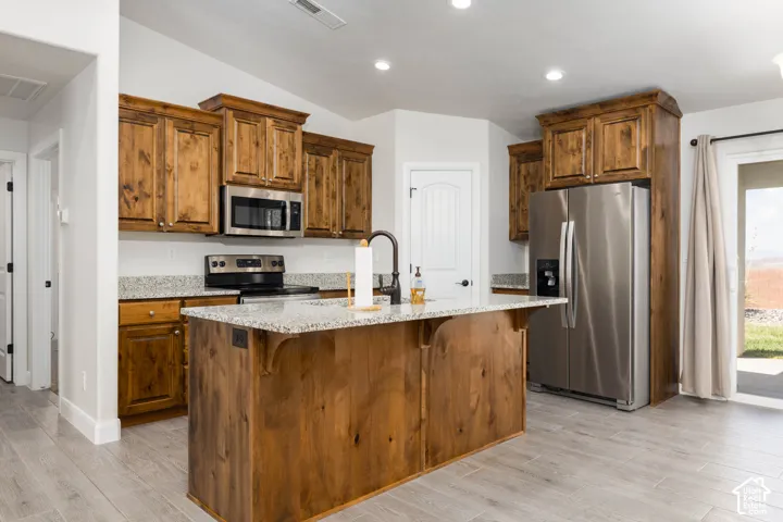 Kitchen featuring wood cabinetry, stainless steel appliances, a center island with a stone-finish countertop, and light-tone wood-finish flooring