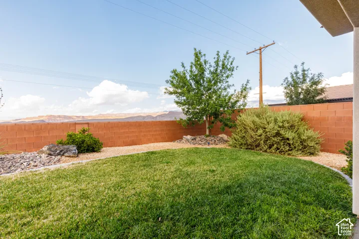 Expansive backyard featuring a manicured lawn, a concrete block privacy wall, and mature landscaping