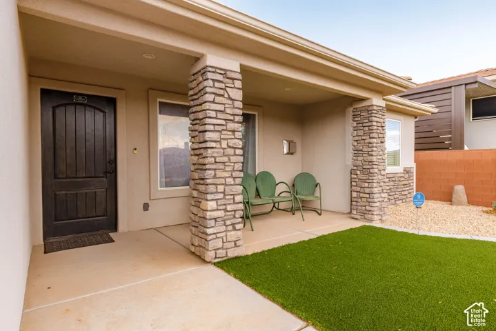 Covered porch with stone-clad columns, a dark wood-paneled entry door, and a synthetic lawn area