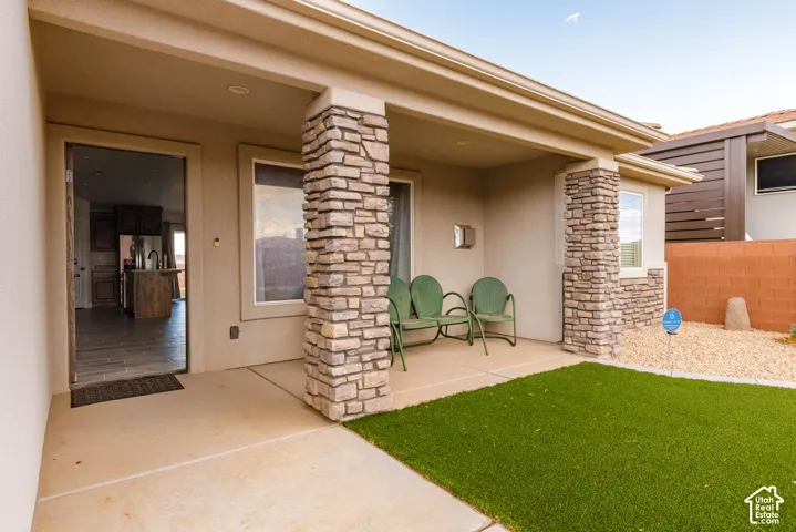 Covered patio with stone-accented pillars, concrete flooring, artificial turf, and a gravel bed