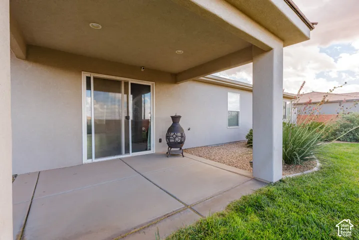 Covered patio with recessed lighting, concrete flooring, sliding glass doors, and a grass lawn with landscaped rock features
