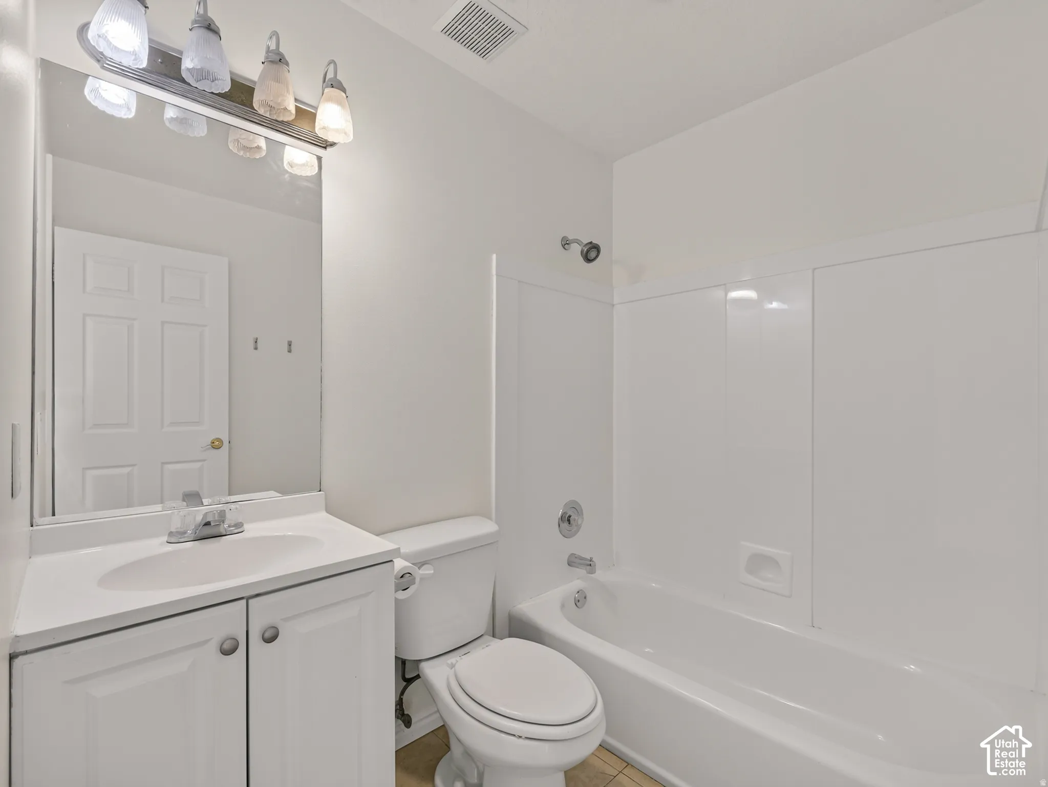 Bathroom featuring a vanity with a white countertop and integrated sink, a built-in bathtub with a shower, and a medicine cabinet with an attached light fixture