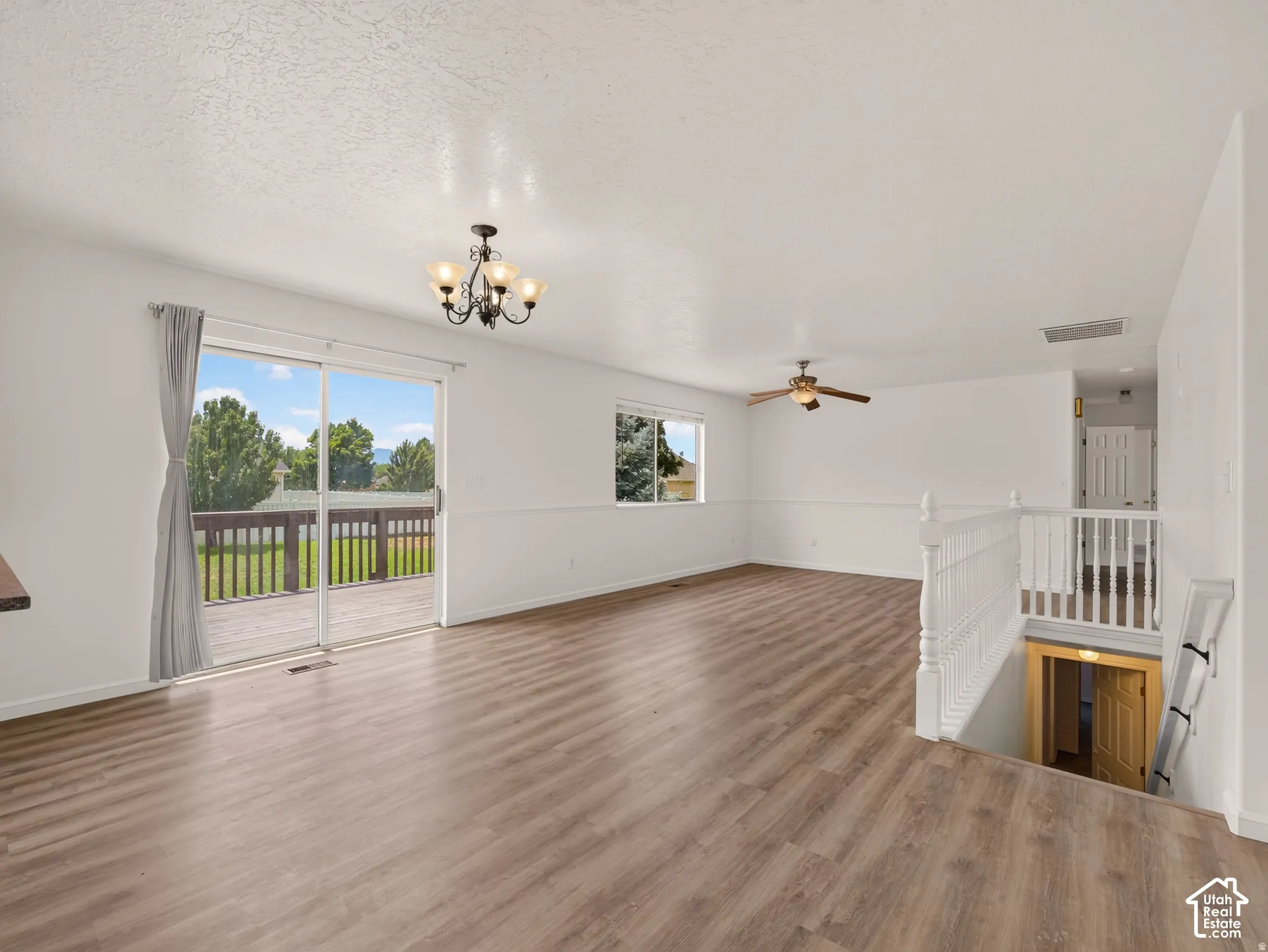 Wood-finish flooring, sliding glass door, overhead chandelier, ceiling fan, and white painted railing