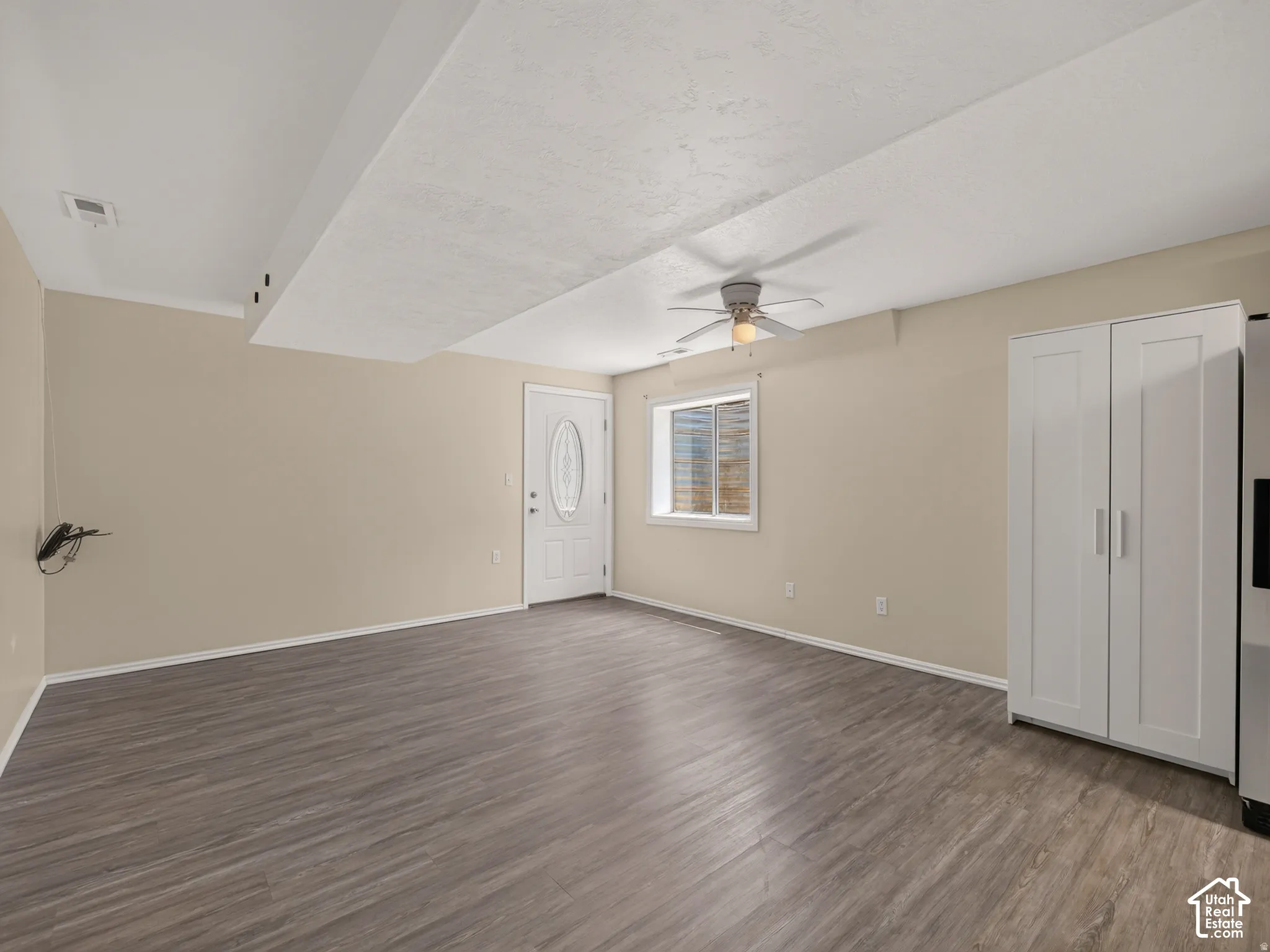 Wood-finish flooring, recessed lighting, and a ceiling fan are featured in this space with a white paneled door with decorative glass