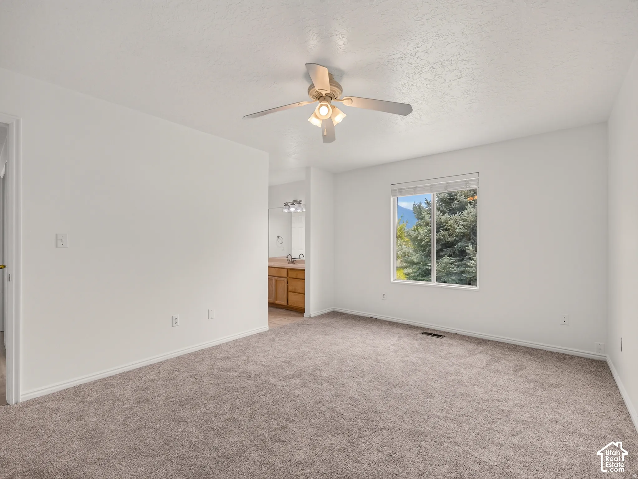 Carpeted room with a ceiling fan, a window, and a partial view of a bathroom vanity with dual sinks