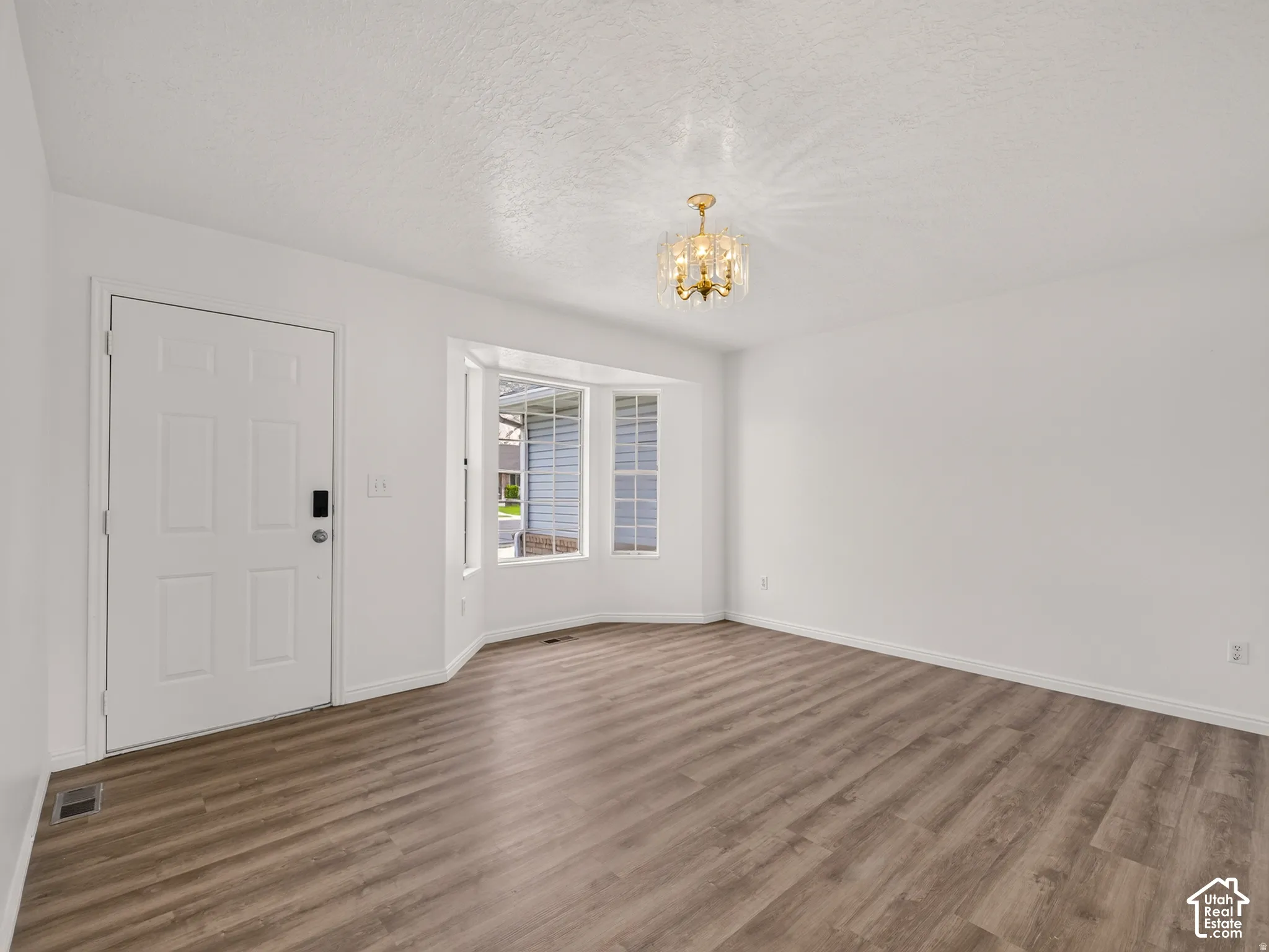 Wood-finish flooring, bay window, white paneled door, flush-mount chandelier, and neutral wall tones