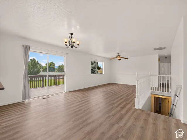 Wood-finish flooring, sliding glass door, overhead chandelier, ceiling fan, and white painted railing