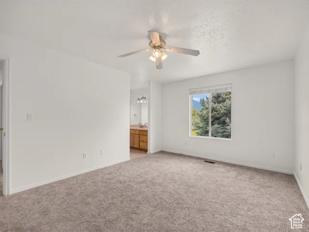 Carpeted room with a ceiling fan, a window, and a partial view of a bathroom vanity with dual sinks