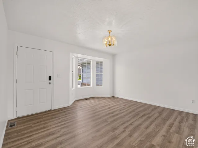 Wood-finish flooring, bay window, white paneled door, flush-mount chandelier, and neutral wall tones