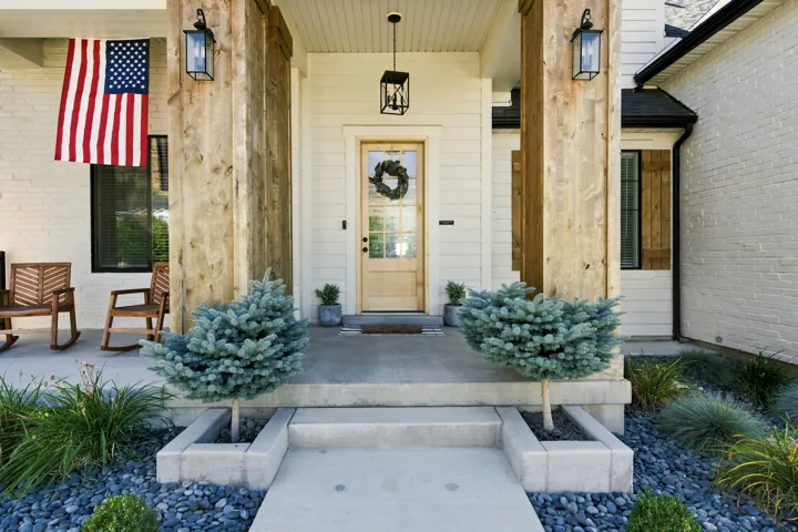 Front entry featuring substantial wood-wrapped columns, a natural wood-finish door with glass panels, white siding, and brick facade