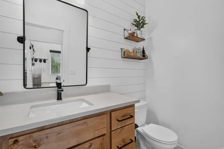 Wood-finish vanity with drawer storage, white stone-finish countertop, rectangular undermount sink, and matte black faucet