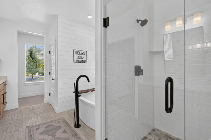 Glass-enclosed shower with subway tile surround, standalone soaking tub with floor-mounted faucet, and wood-finish vanity