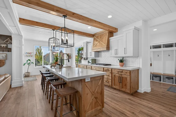 Open-concept kitchen featuring wood-finish flooring, a large island with seating, white shaker-style upper cabinetry, natural wood lower cabinetry, and a white subway tile backsplash