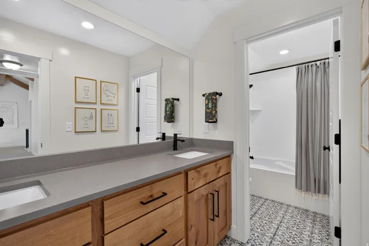 Double vanity with integrated sinks, gray countertop, natural wood-finish cabinetry, and matte black fixtures