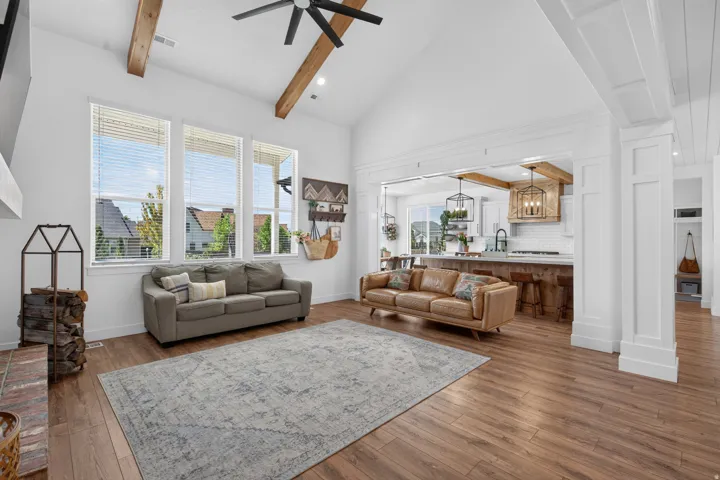 Vaulted ceilings with exposed wood beams, wood-finish flooring, and white walls create a bright interior