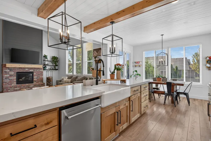 Vaulted ceiling with exposed wood beams, brick fireplace with wood mantel, wood-finish flooring, white farmhouse sink, and large windows