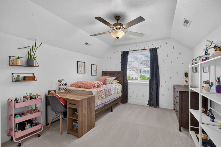 Vaulted ceiling with an attached ceiling fan, large window with blinds, light-toned carpeting, and built-in shelving